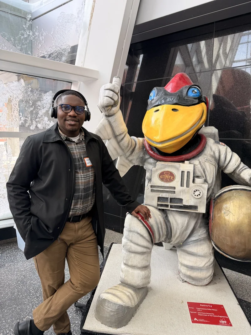 A visitor stands beside Astro Cy, Iowa State’s bird mascot sculpture dressed in a spacesuit and holding a gold helmet.