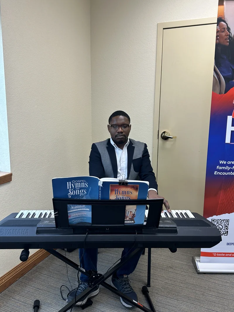 A keyboardist sits behind a Yamaha keyboard with open Gospel Hymns and Songs books on its music stand.