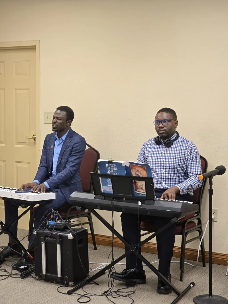 Two musicians seated at electronic keyboards, with gospel hymn books, microphones and audio equipment.