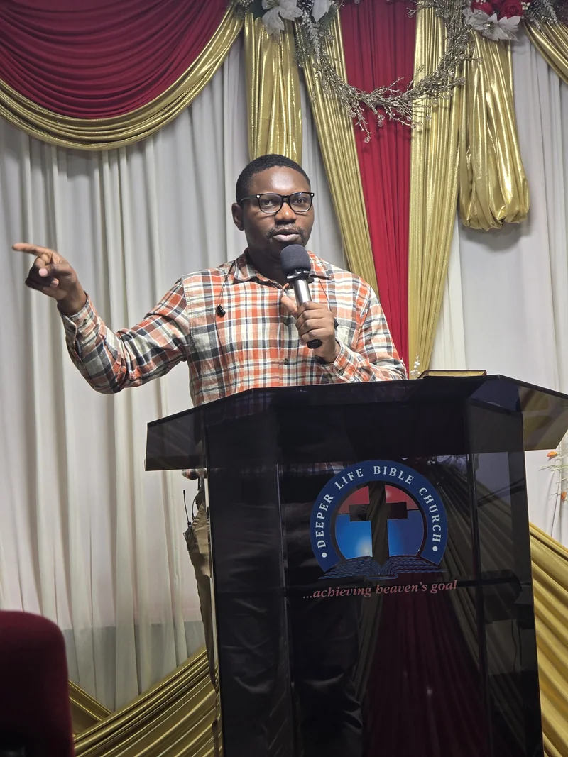 A speaker holds a microphone and gestures from behind a lectern bearing the Deeper Life Bible Church emblem.
