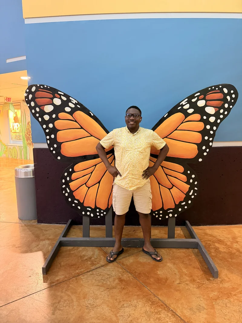 A visitor poses in front of oversized orange, black and white butterfly wings against a blue wall.